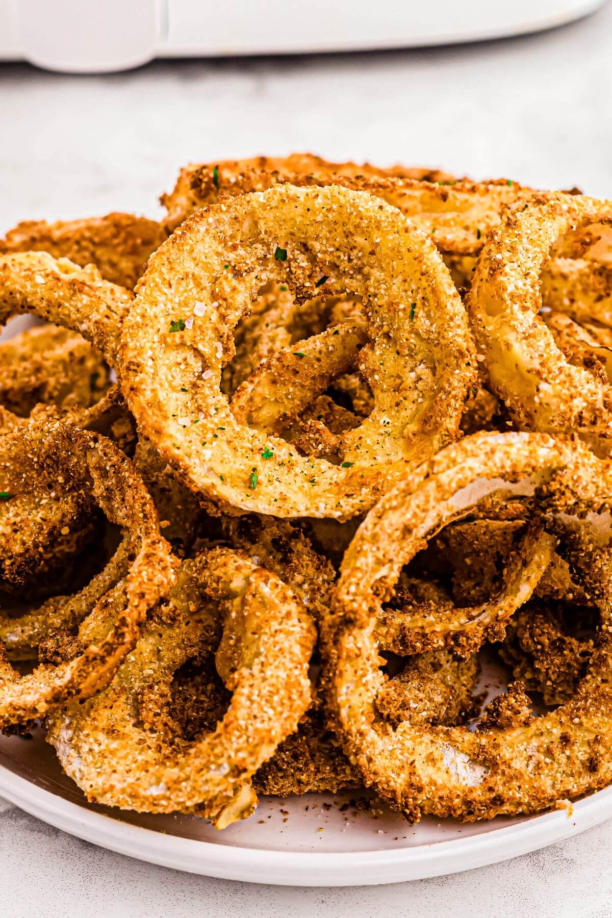 Golden crispy battered onion rings stacked on a white plate. 