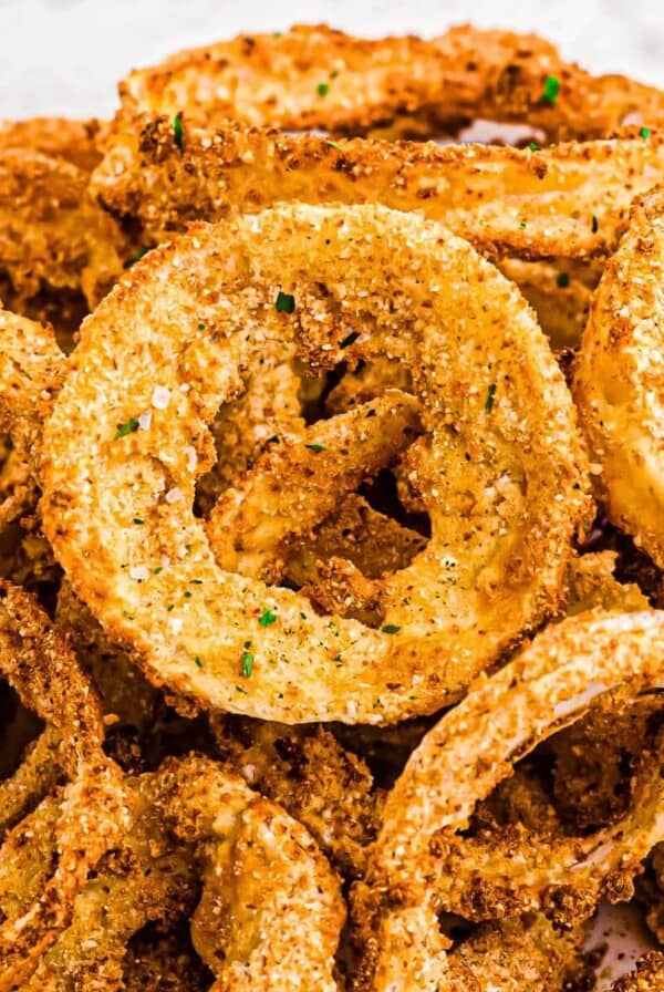 Golden crispy battered onion rings stacked on a white plate.