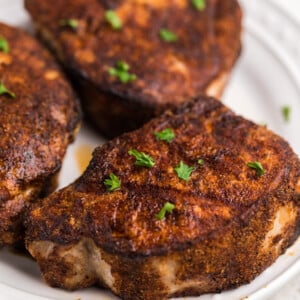 Pork chops on a white plate and topped with parsley.