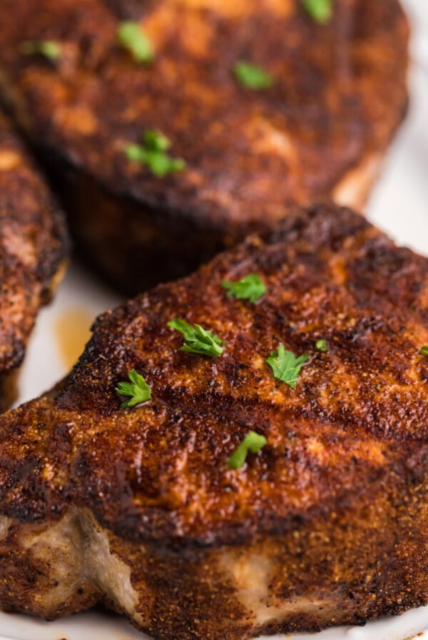 Pork chops on a white plate and topped with parsley.