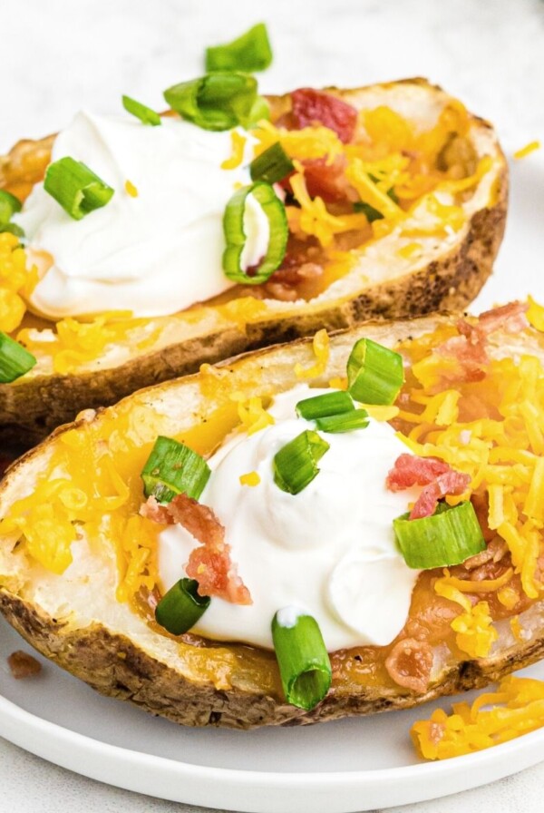 Potato skins topped with sour cream, cheese, bacon, and green onion, served on a white plate