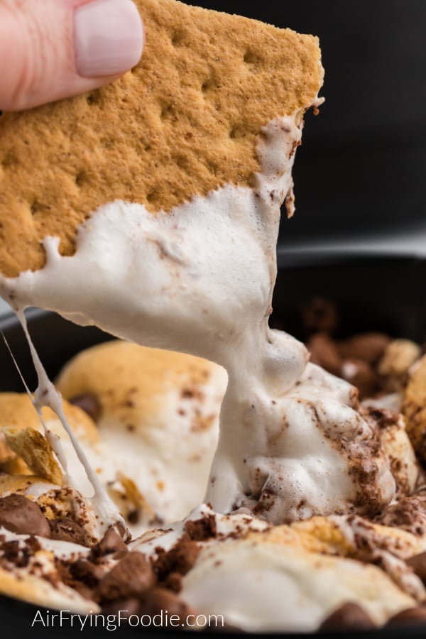 Graham Cracker being dipped into gooey marshmallow and chocolate S'mores Dip that was made in the Air Fryer. 