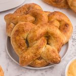 Golden soft pretzels served on a white plate, sprinkled with sea salt and melted cheese.