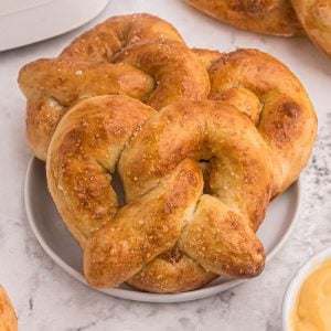Golden soft pretzels served on a white plate, sprinkled with sea salt and melted cheese.