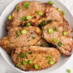 Juicy pork chops cooked and served in a white shallow bowl. Sprinkled with green onions and sesame seeds.
