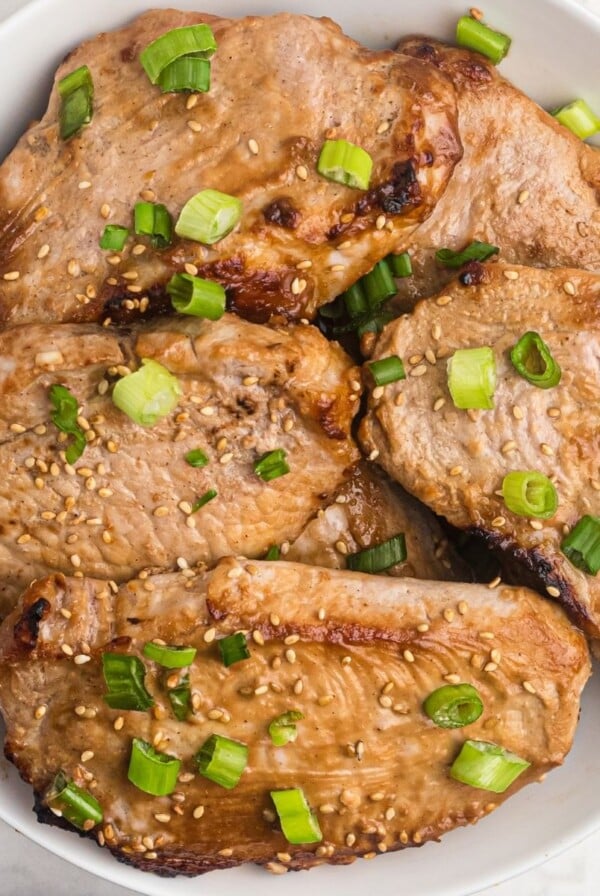 Juicy pork chops cooked and served in a white shallow bowl. Sprinkled with green onions and sesame seeds.