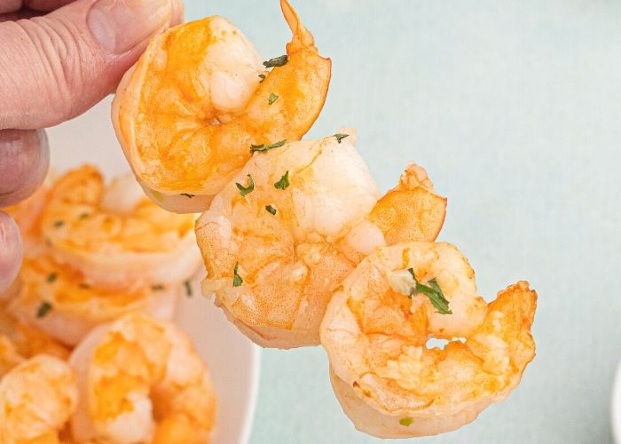 Golden air fryer shrimp, cooked and served on on a skewer, and seasoned with garlic.