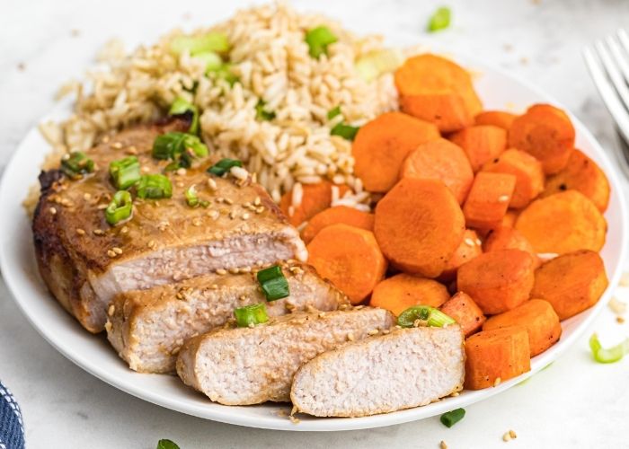 Juicy pork chops cut into slices, served with carrots and rice on a white plate. 