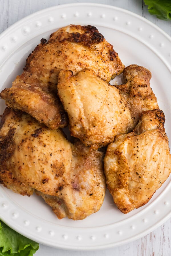 overhead photos of chicken thighs fully cooked in the air fryer and served on a white plate.