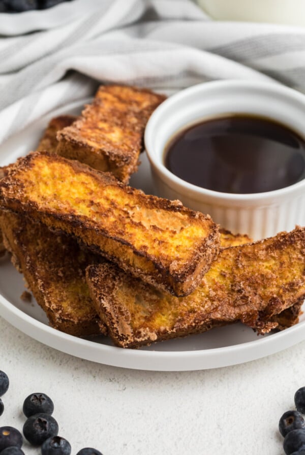 French toast sticks made in the air fryer on a white plate with blueberries surrounding it.