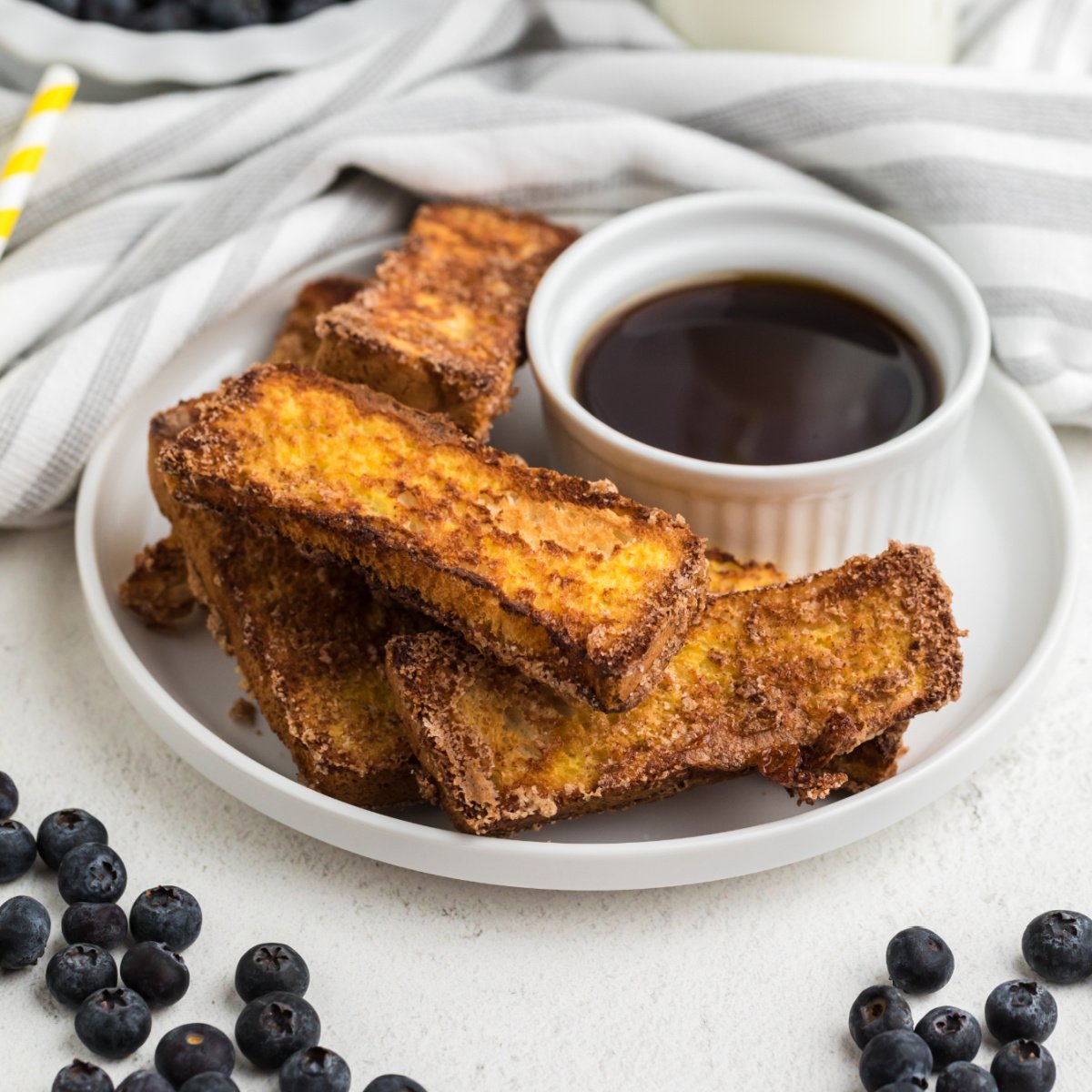 French toast sticks made in the air fryer on a white plate with blueberries surrounding it.
