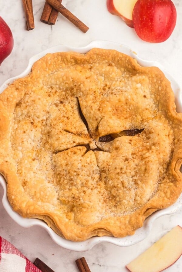 Golden baked apple pie, with red apples and red and white straws on the table.