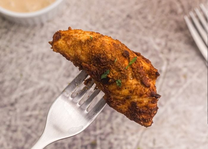Up close photo of piece of seasoned chicken on a fork garnished with parsley flakes. 
