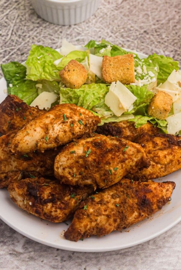 Blackened chicken served on a white plate with a salad.