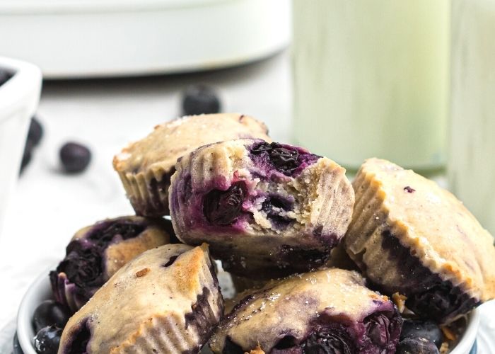 Mini muffins stacked with a bite taken. Milk and fresh blueberries on the table. 