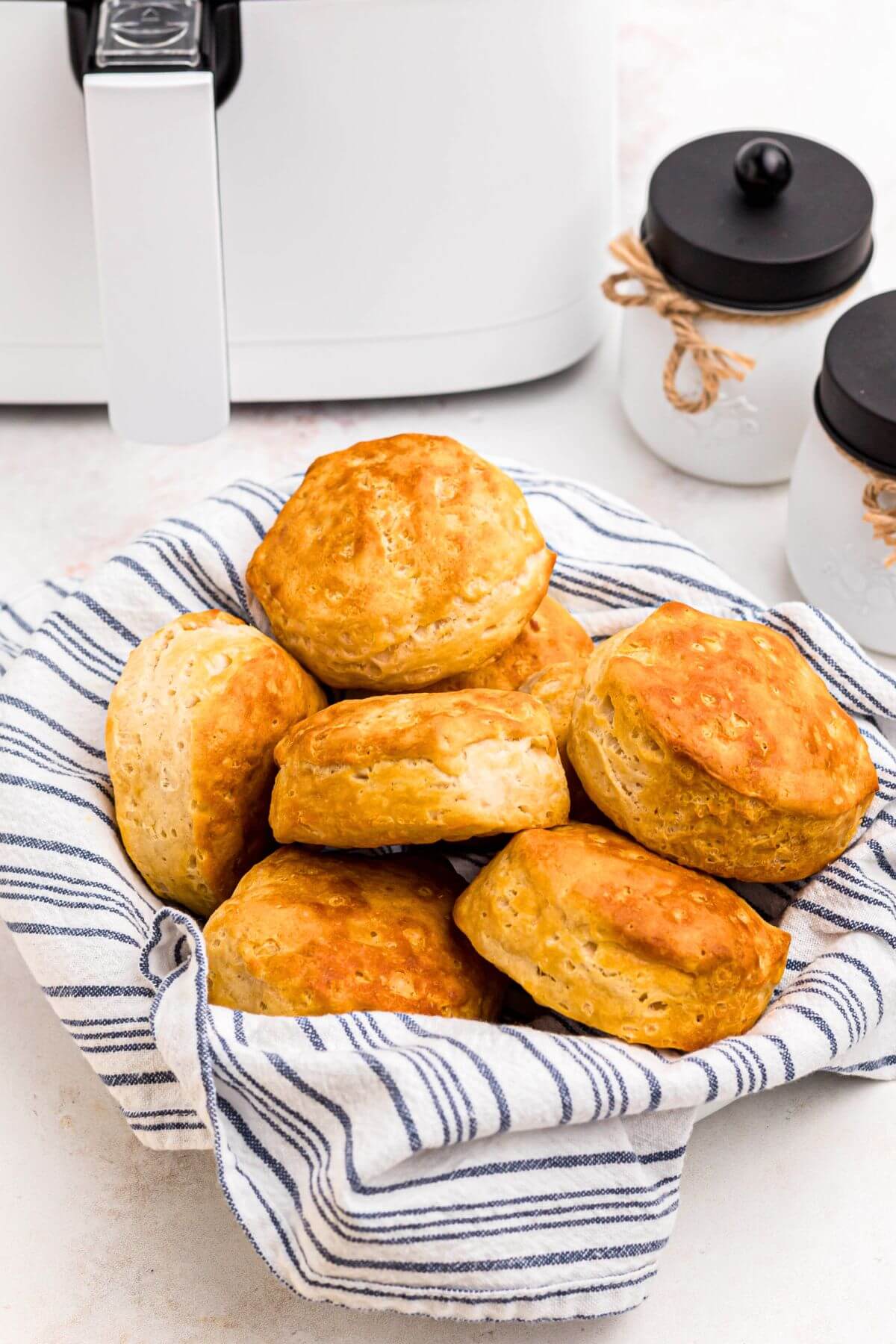 Golden biscuits stacked in a basket in front of the air fryer. 