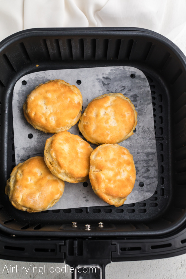 Biscuits on a sheet of parchment paper in the air fryer basket. 