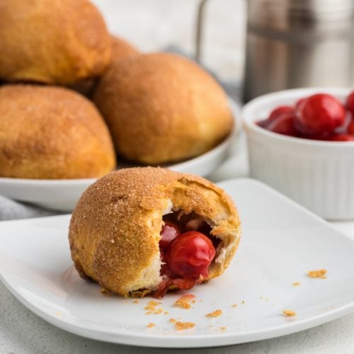 Air Fryer Cherry Pie Bomb with a bite taken out of it on a white plate.