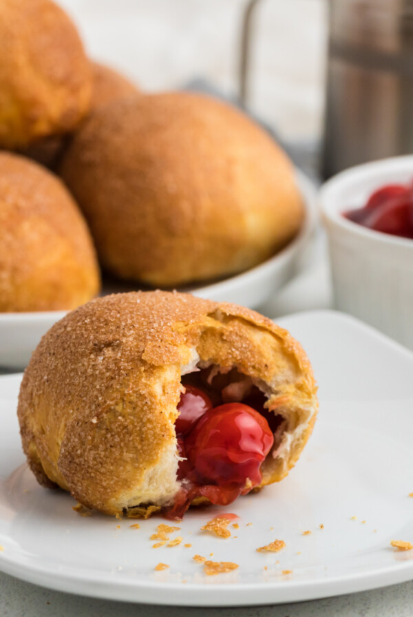 Air Fryer Cherry Pie Bomb with a bite taken out of it on a white plate.