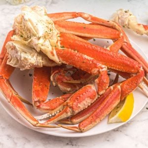 Orange crab legs on a white plate, served with lemon slices and sprinkled with parsley flakes.