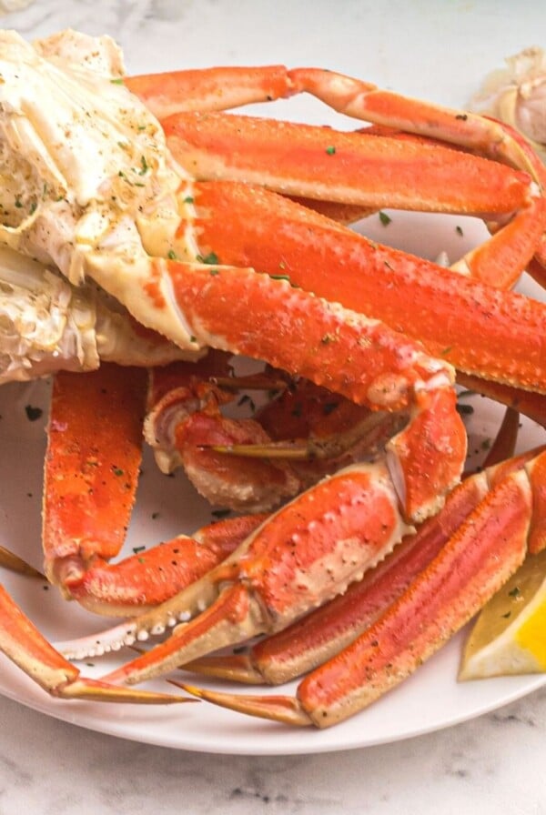 Orange crab legs on a white plate, served with lemon slices and sprinkled with parsley flakes.