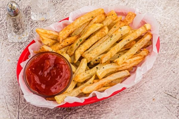 Crispy golden french fries in a red basket, seasoned and served with ketchup. 