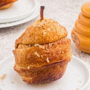 Golden pear wrapped in a puff pastry, sprinkled with brown sugar and served on a white plate.
