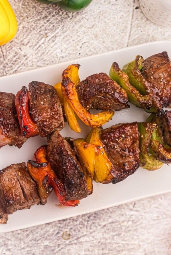 Steak kabobs with vegetables on a white plate with bell peppers scattered on the table.