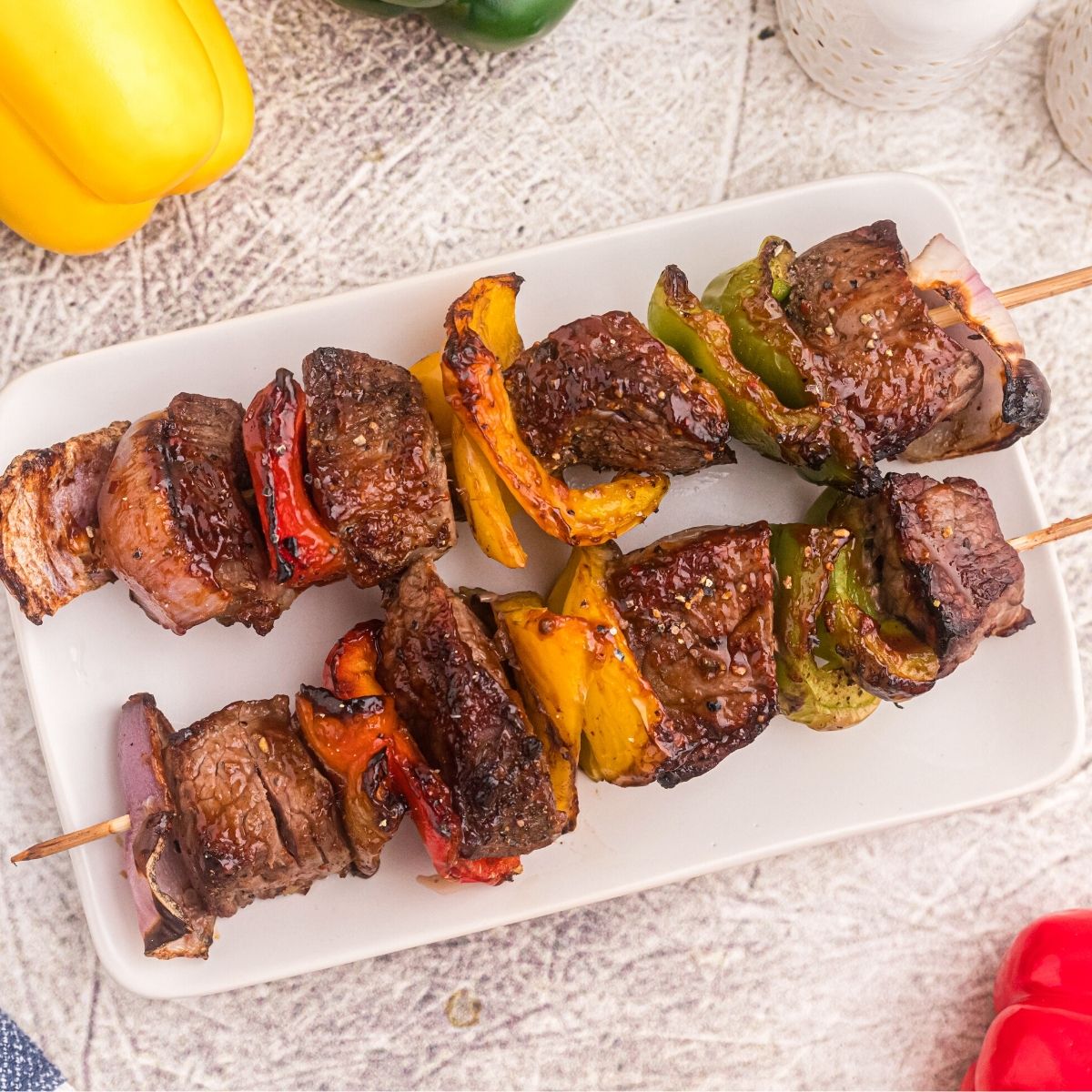 Steak kabobs with vegetables on a white plate with bell peppers scattered on the table.