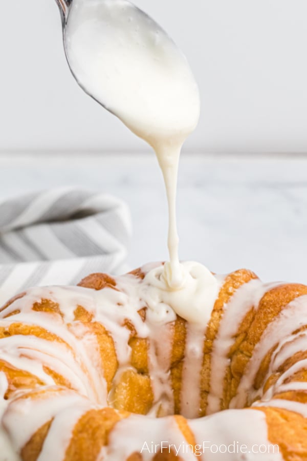 Glaze being drizzled from a spoon onto monkey bread made in the Air Fryer. 
