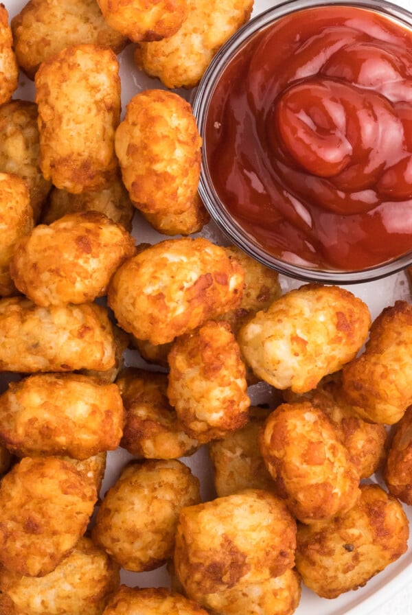 Tater Tots on a white plate that were made in the Air Fryer. A small bowl of ketchup on the side.