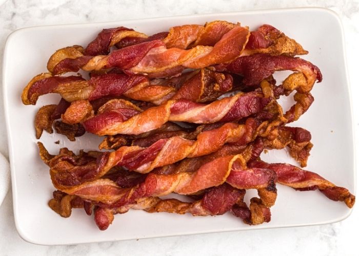 crispy twisted bacon on a white rectangle plate, stacked on top of each other. 