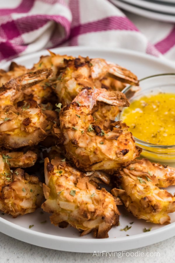Close up shop of keto coconut shrimp on a white plate with a buttery dipping sauce on the side. 