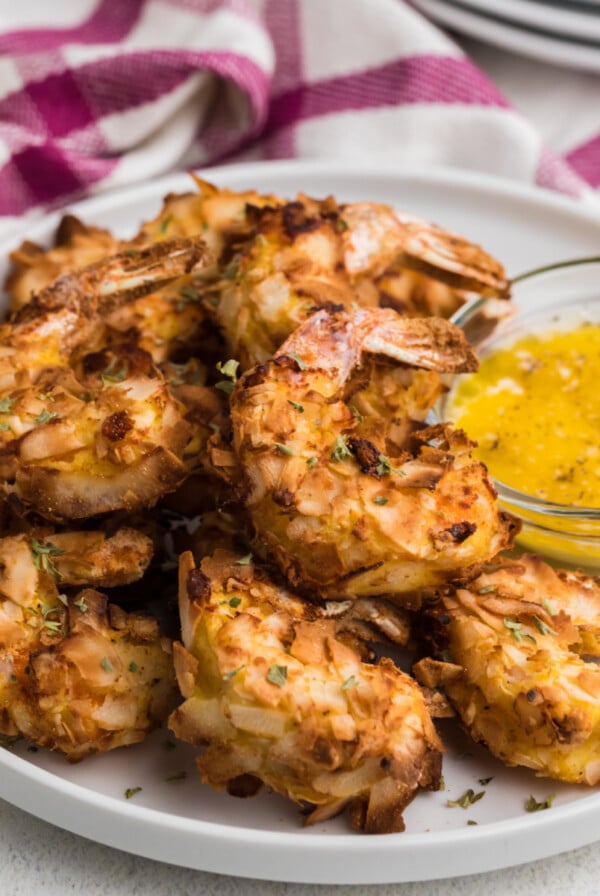 Air Fryer Keto Coconut Shrimp on a white plate ready to eat with a side of buttery dipping sauce to serve.