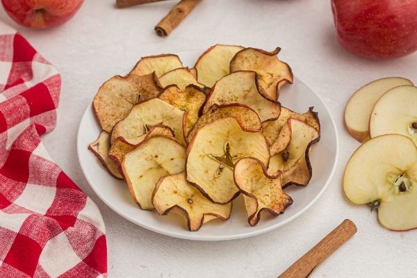Golden yellow apple chips, stacked and served on a white plate. 
