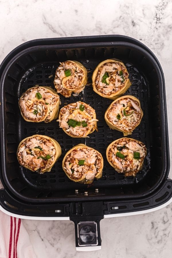 Uncooked rolled air fryer BBQ chicken pizza roles in the air fryer basket.