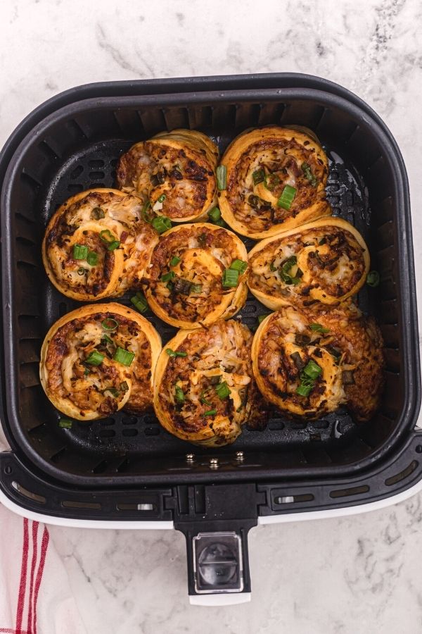 Cooked air fryer BBQ chicken pizza roles in the air fryer basket, sprinkled with chopped green onions. 