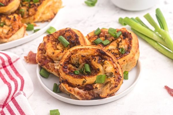 Golden bbq rolls with chicken and sauce, topped with chopped green onions on a white plate. 
