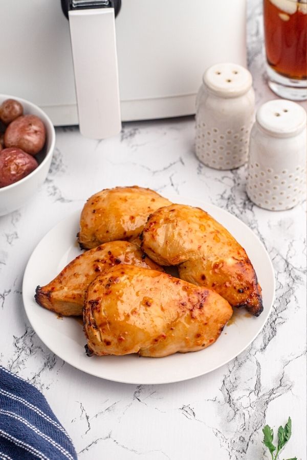 Golden chicken breasts in front of an air fryer served on a white plate. 