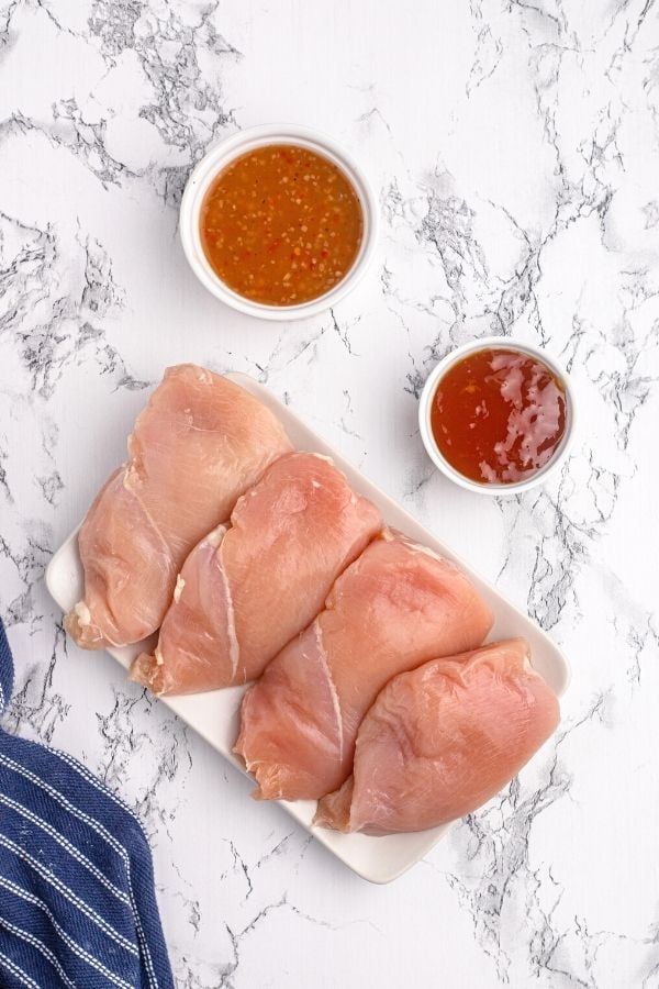 Ingredients to make glazed chicken on a white plate. Raw chicken, Italian dressing, and peach preserves. 