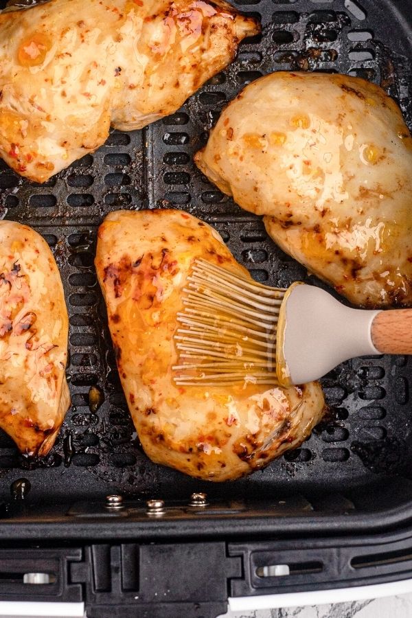 Chicken in the air fryer basket being brushed with peach glaze.