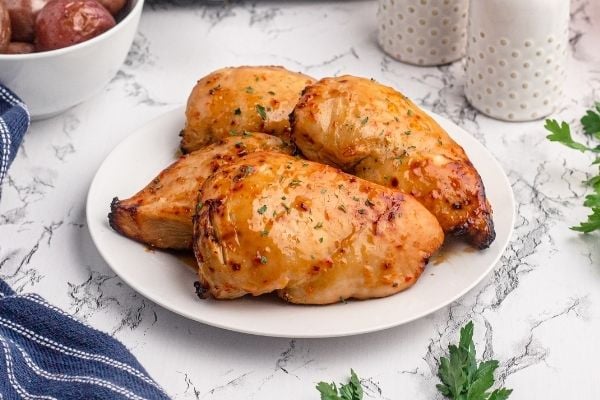 Golden glazed chicken breasts, on a white plate sprinkled with dried parsley on a marble table. 