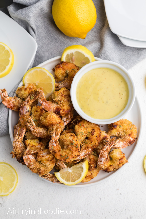 Keto fried shrimp made in the air fryer on a white plate with lemon slices and dipping sauce - ready to serve. 