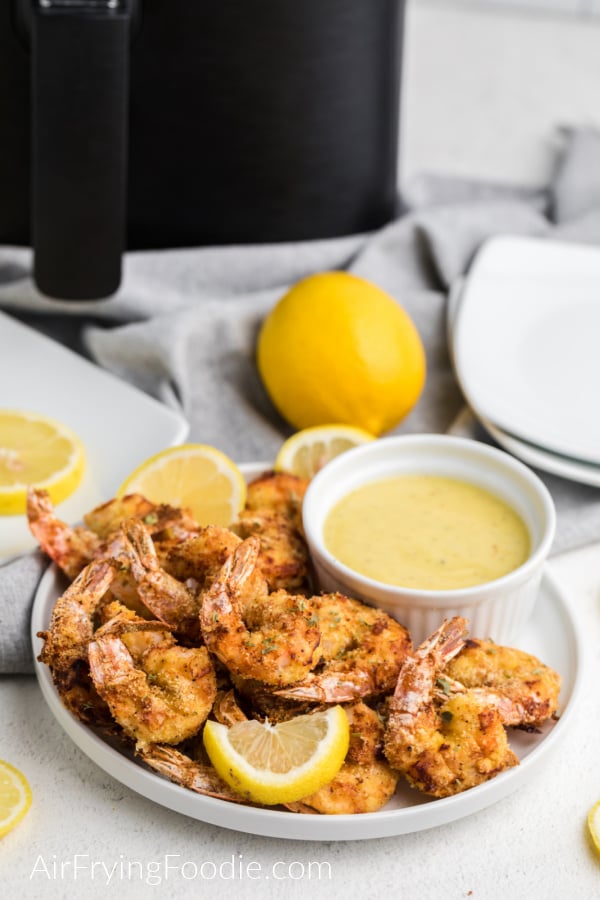 Keto Fried Shrimp made in the air fryer on a white plate with lemon slices and a dipping sauce on the side. 