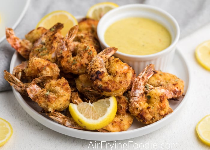 Air Fryer keto Fried Shrimp on a white plate ready to eat - served with lemon slices and a dipping sauce. 