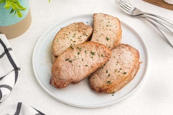 Glazed pork chops on a white plate garnished with parsley flakes. 