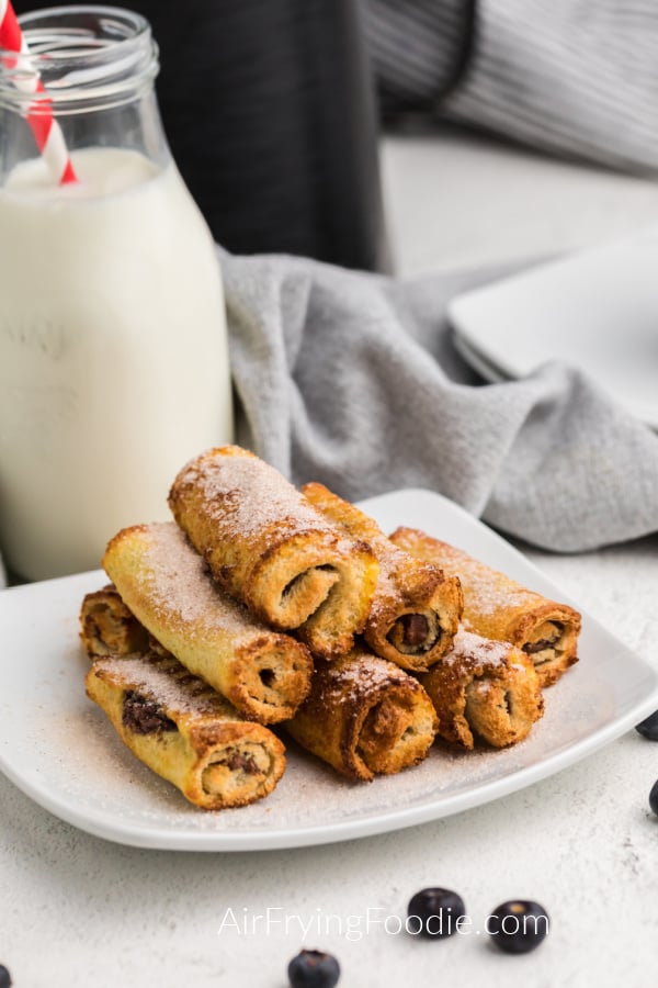 Nutella French Toast Rolls Ups on a white plate in front of the Air Fryer. 