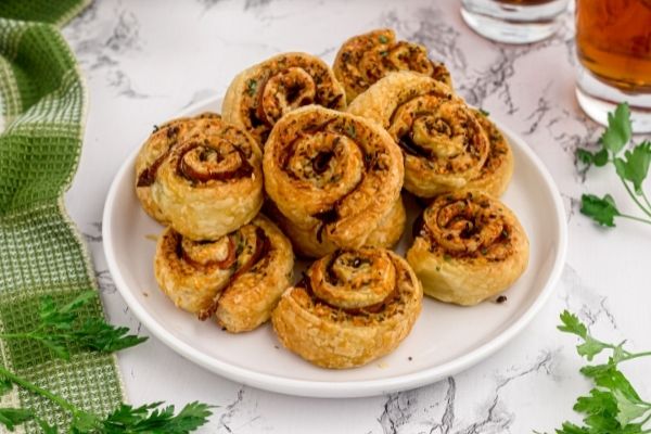 Golden pesto pinwheels piled on a white plate, garnished with parsley.
