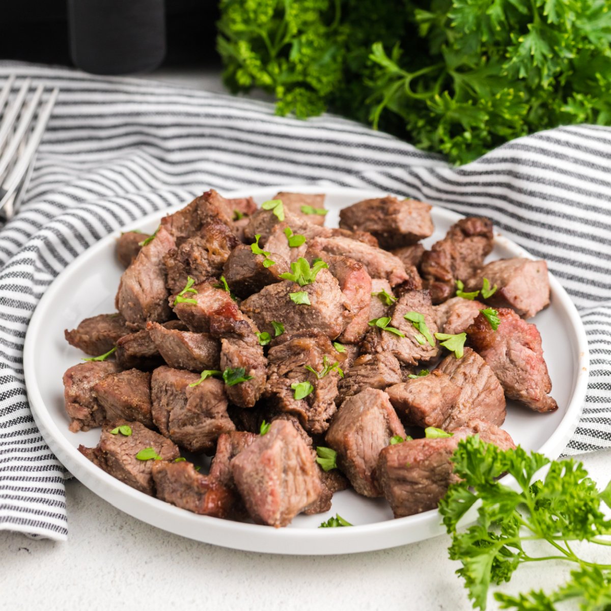 steak bites made in the air fryer and served on a white plate and topped with fresh parsley.