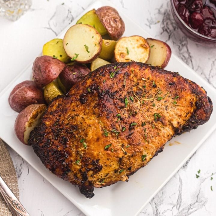 Close up photo of golden crispy turkey breast on a white plate and served with baby potatoes.